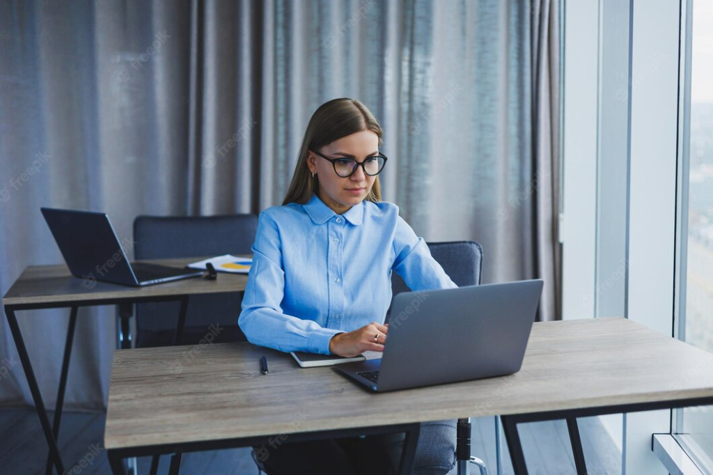 a-beautiful-woman-in-glasses-sits-at-a-table-in-the-office-and-works-at-a-laptop-corporate-work-in-the-office-modern-woman-workplace-manager-in-classic-clothes_173815-30739.jpg